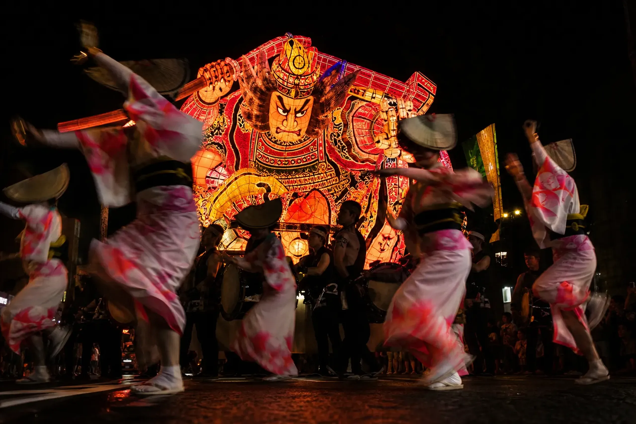 Illuminated Nebuta float with haneto dancers and taiko drums during the Aomori Nebuta Festival night parade