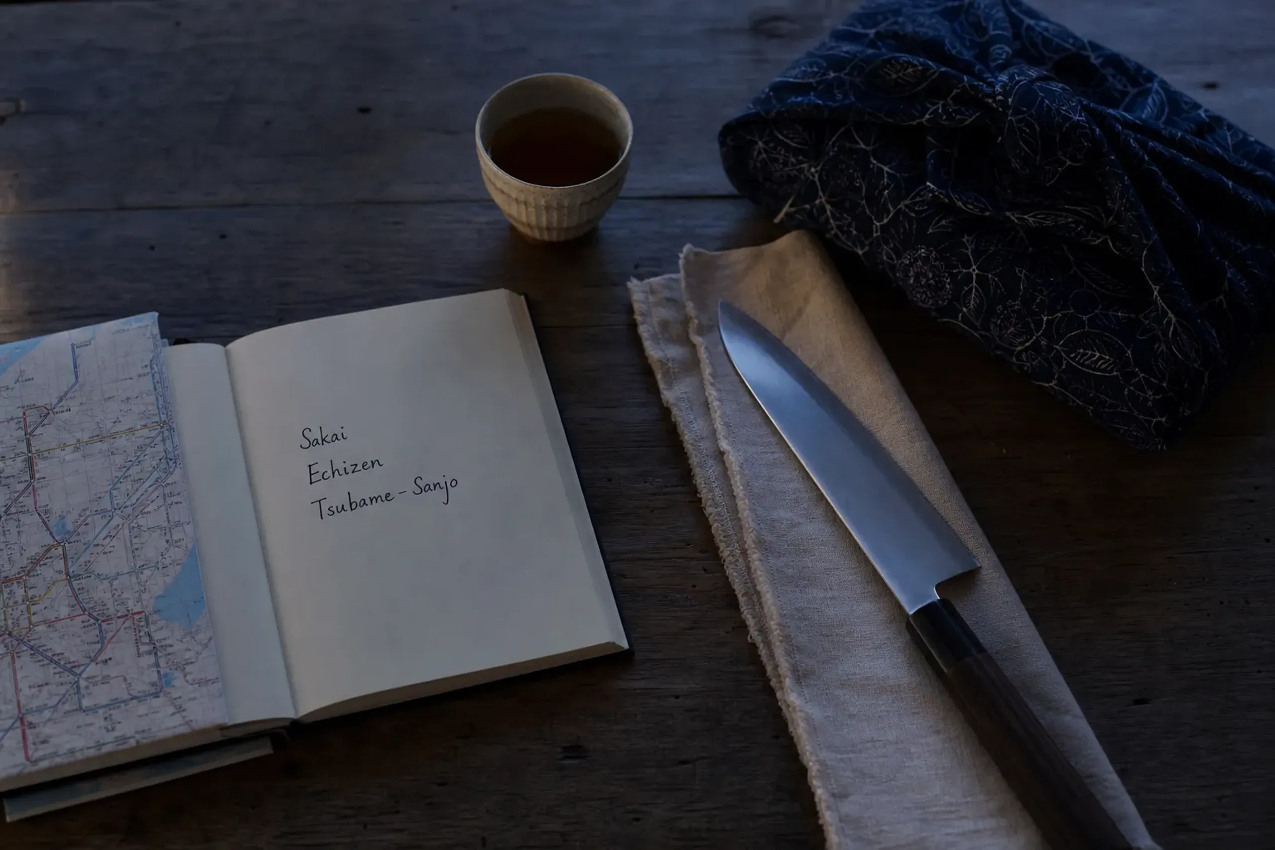 Notebook route notes for Sakai, Echizen, and Tsubame-Sanjo beside a Japanese chef knife