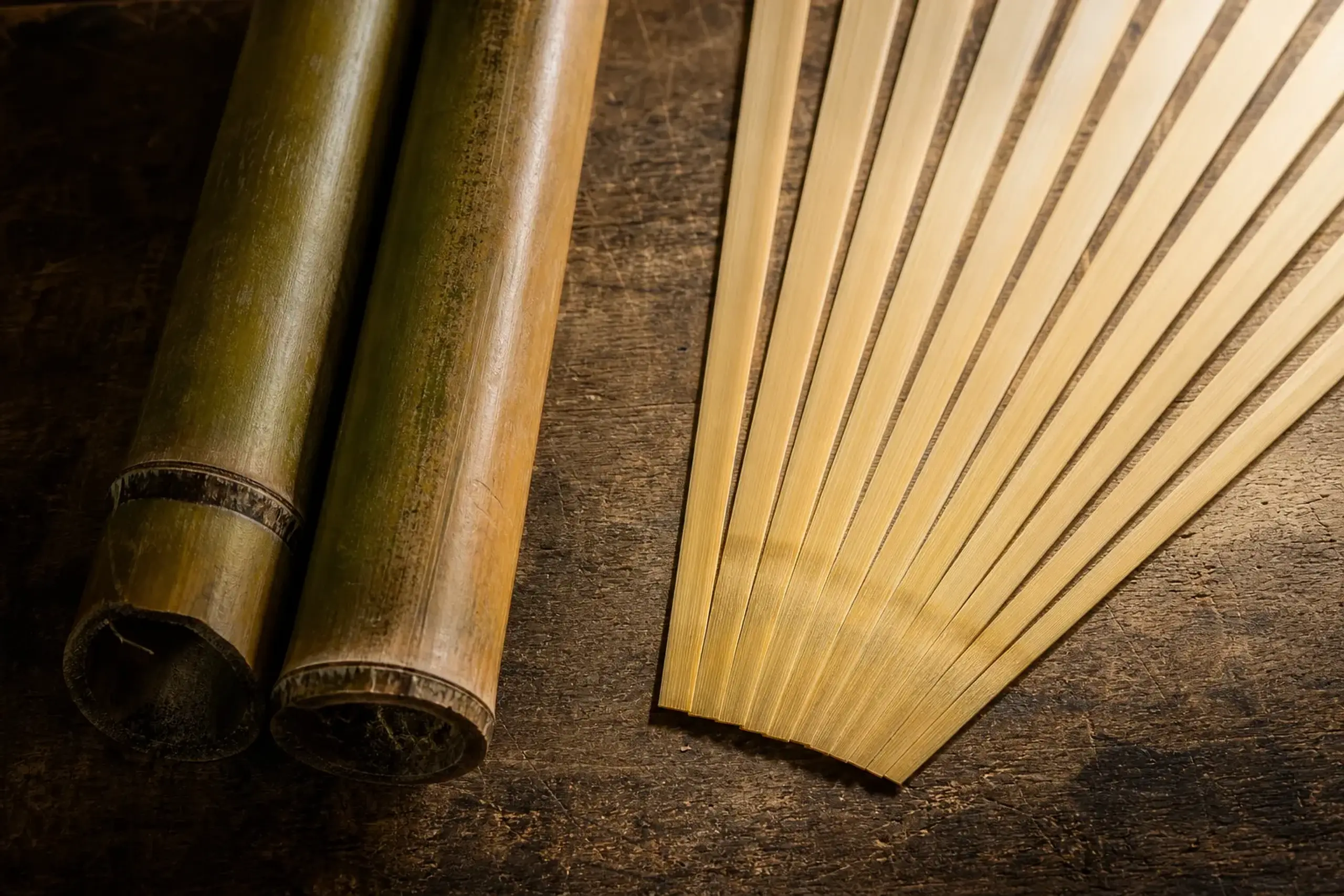 Macro photo showing the precise difference between raw madake bamboo stalks and a collection of uniform, paper-thin, split bamboo strips ready for weaving.