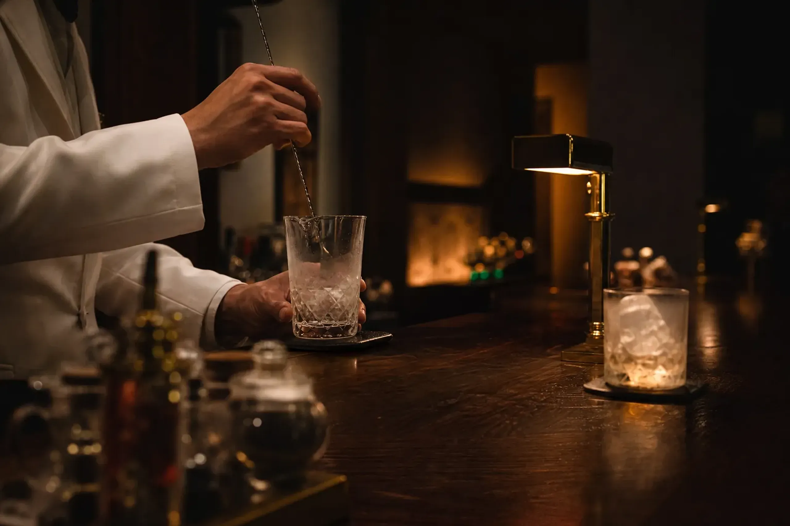 Bartender preparing a cocktail at a dark wood counter in a classic dimly lit hotel bar