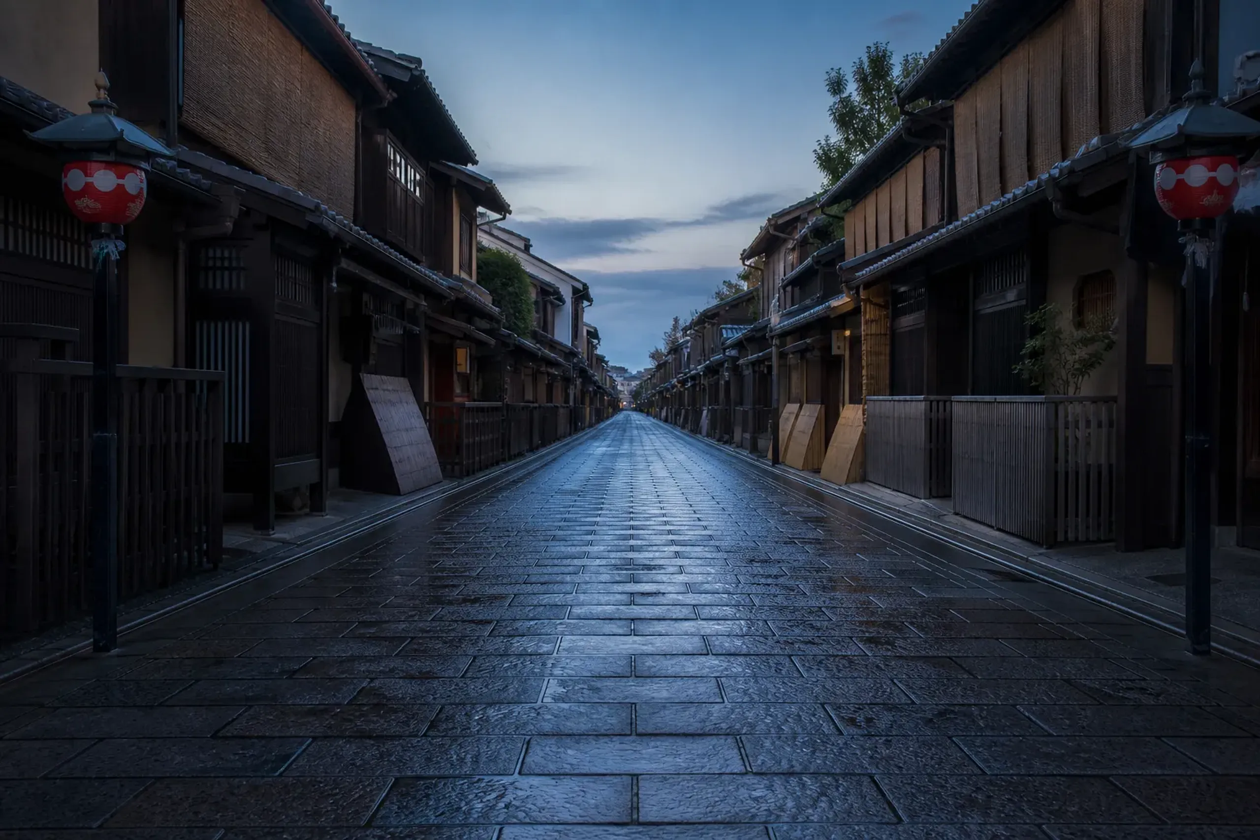 a narrow traditional stone-paved lane in Gion, Kyoto, lined with wooden machiya townhouses and hanging paper lanterns, empty and quiet in early morning light
