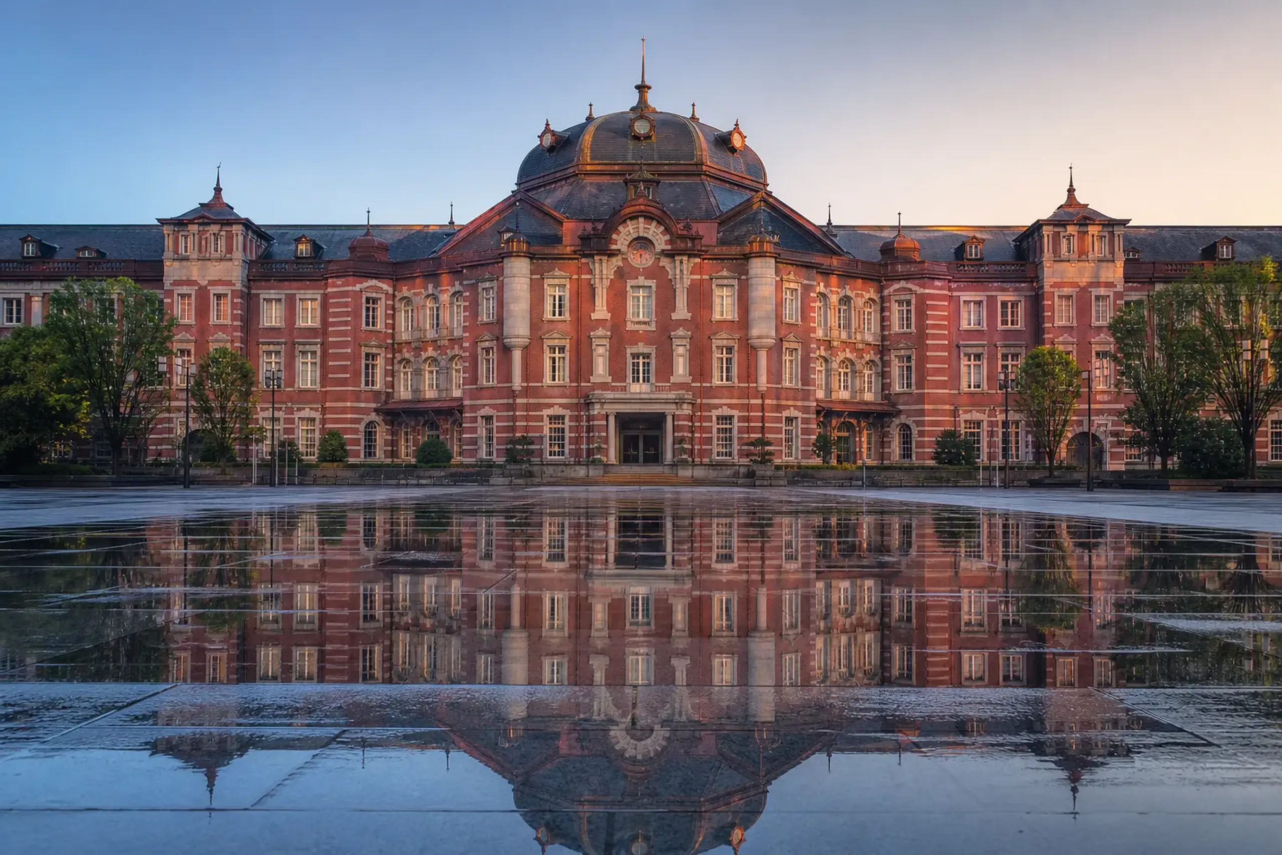 the red-brick facade and central clock dome of Tokyo Station in Marunouchi at dawn, seen across the empty station plaza