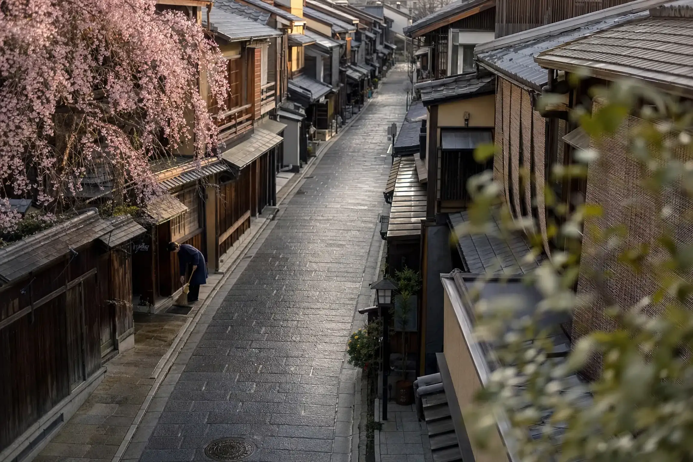 Hanami-koji in Gion Kōbu at early morning, damp stone pavement and shopfronts being swept before the crowds arrive
