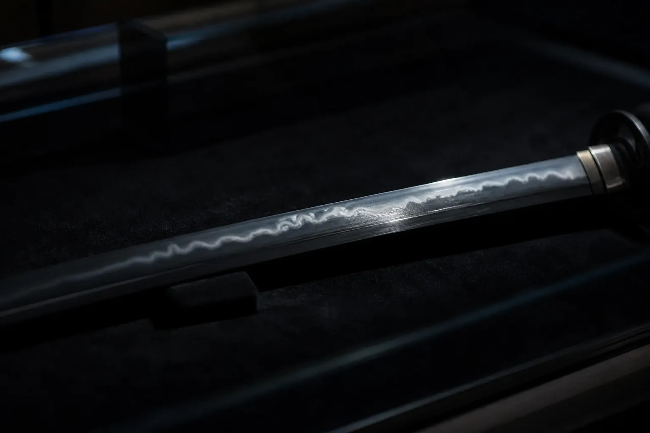 A National Treasure katana displayed behind glass at the Kyoto National Museum, lit to reveal the temper line and steel grain