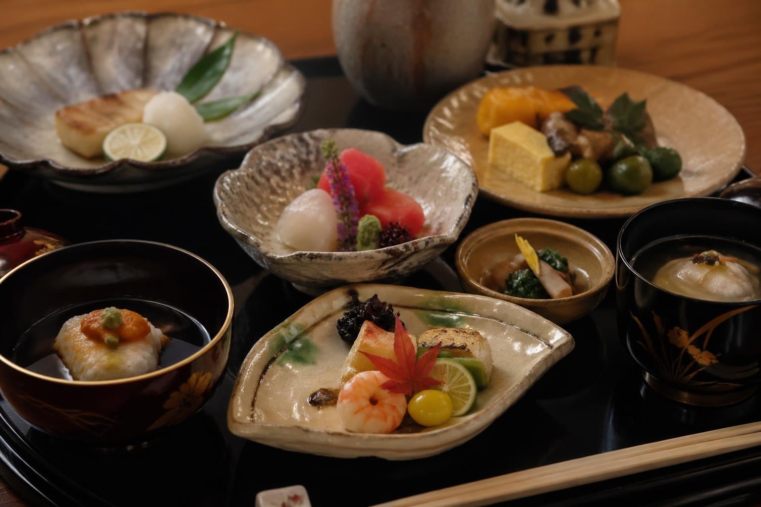 Assorted Japanese kaiseki dishes on a lacquer tray: sashimi, grilled fish, tofu, and vegetables.