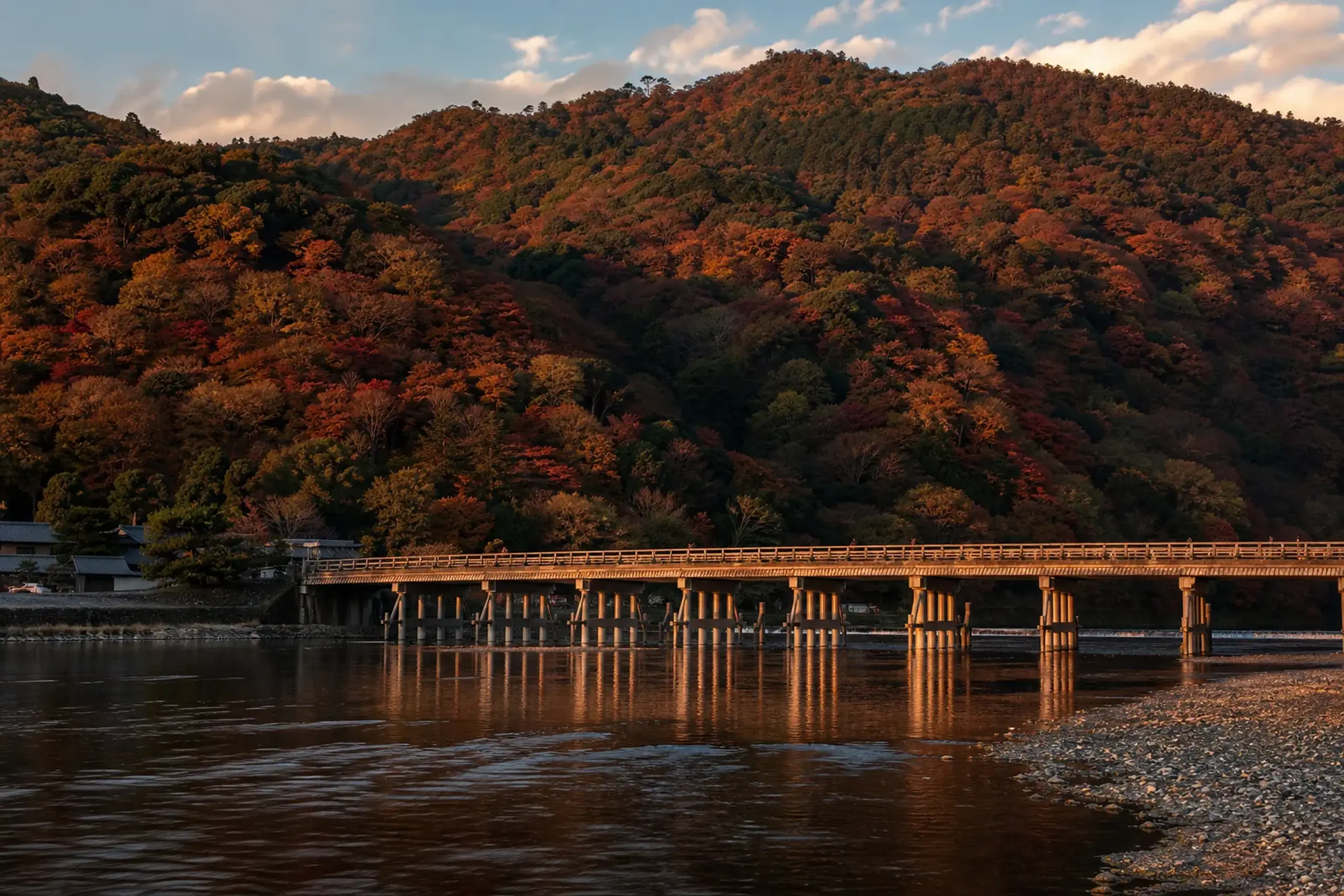 A scenic view of Kyoto's historic Togetsukyo Bridge spanning the Hozu River, with a majestic mountain covered in vibrant autumn foliage in the background.