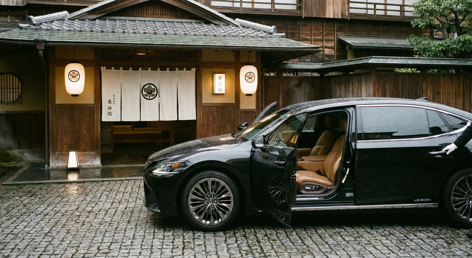 A sleek, black luxury vehicle with its door open, parked in front of a traditional Japanese ryokan entrance.