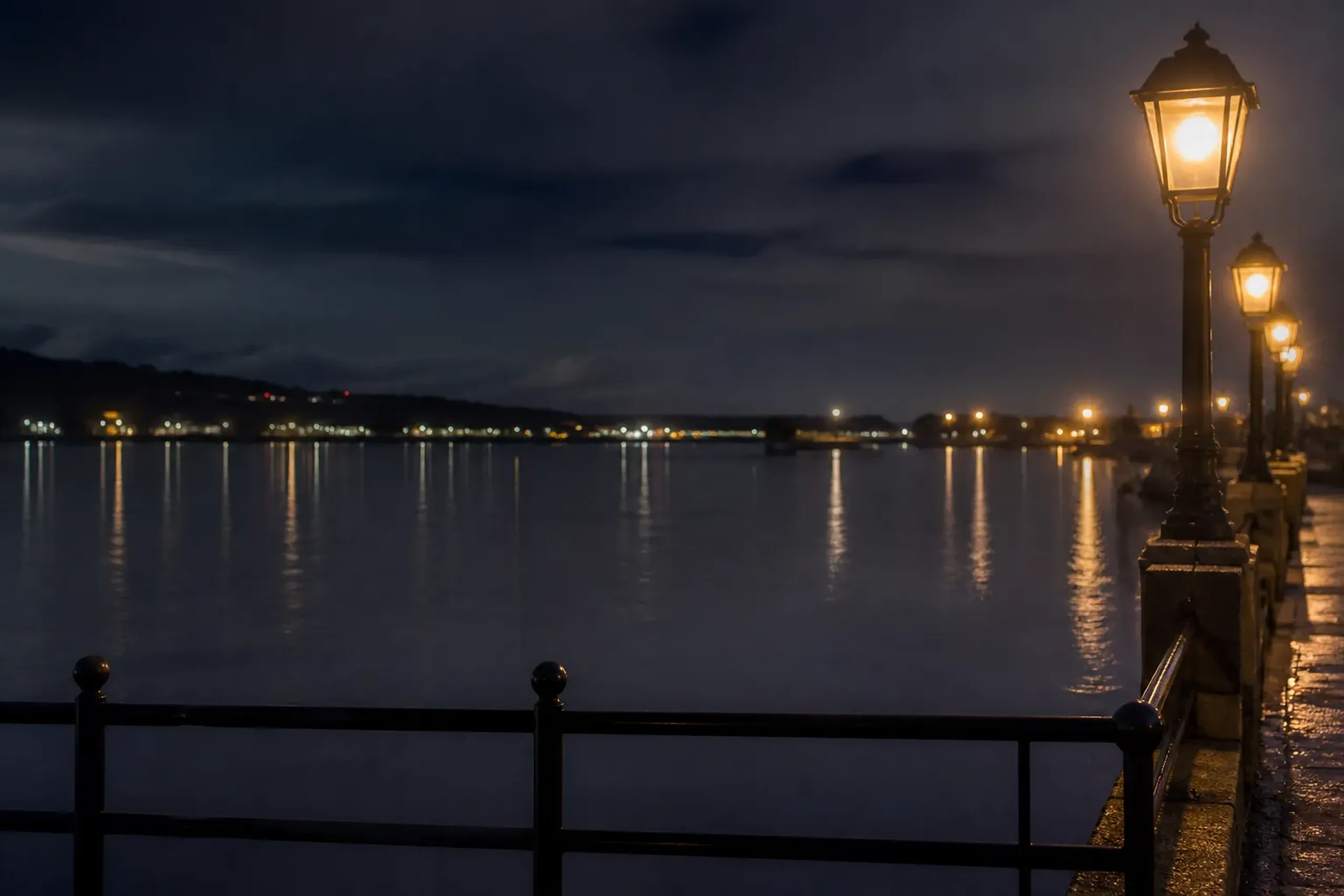 Waterfront harbor at night with reflections and promenade lights, suggesting an evening stroll