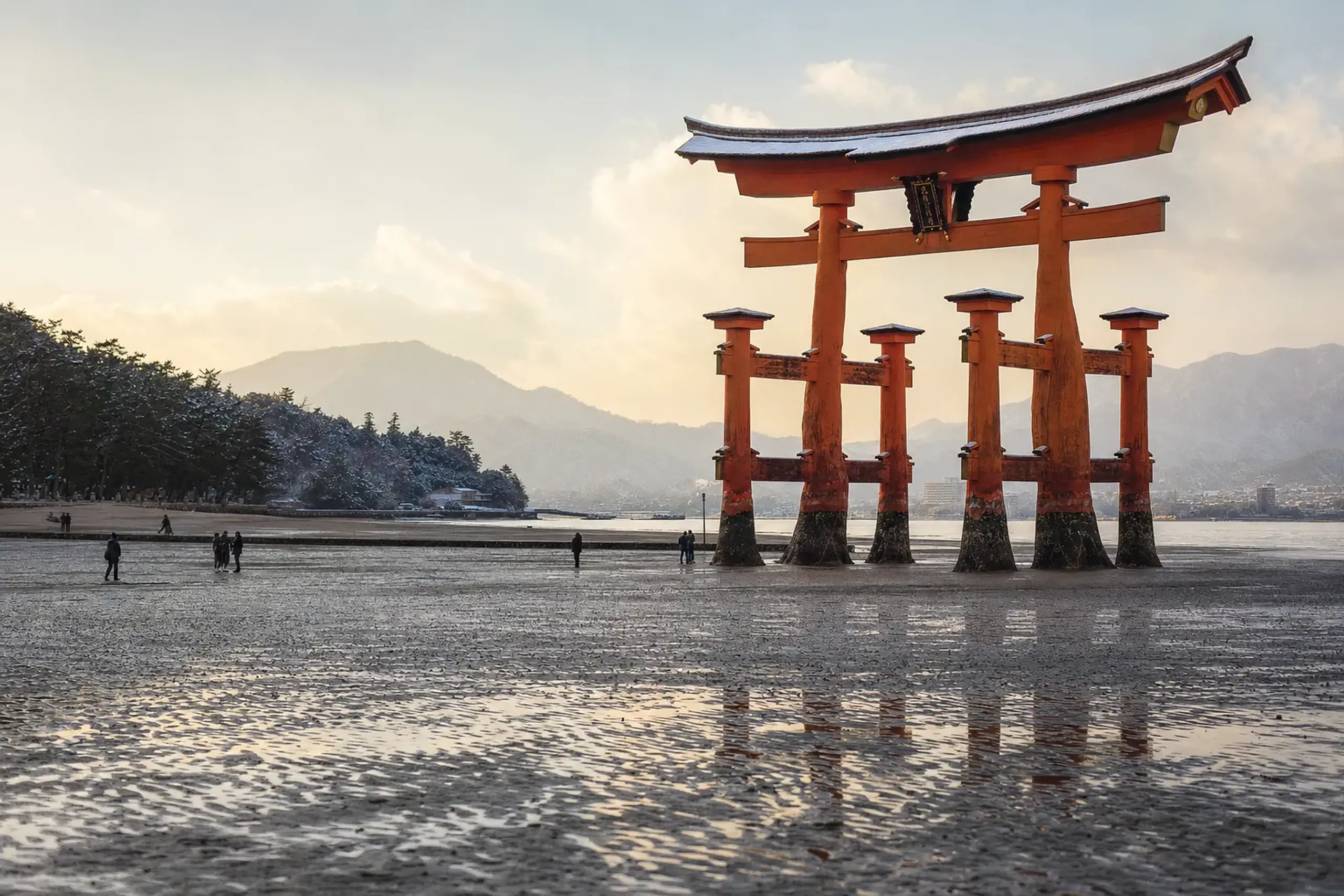the Great Torii of Itsukushima marooned on exposed wet sand at low tide, its pine-pile footings visible in the mudflat
