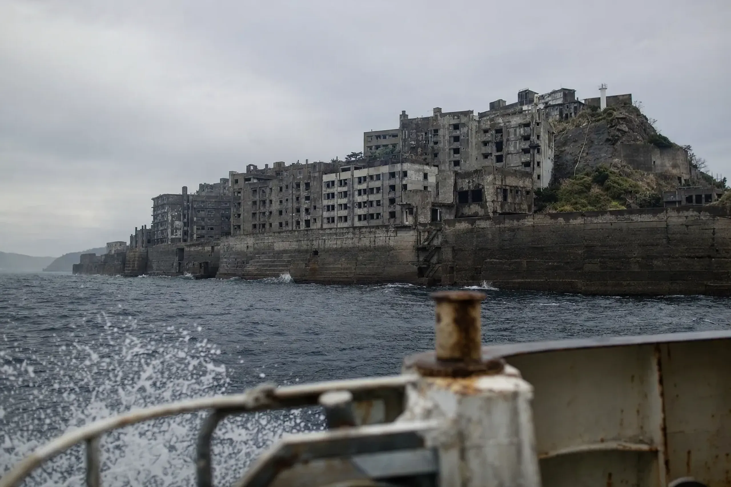The crumbling abandoned concrete apartment blocks of Hashima Island (Gunkanjima) rising from the sea off Nagasaki, seen from the deck of a landing cruise boat