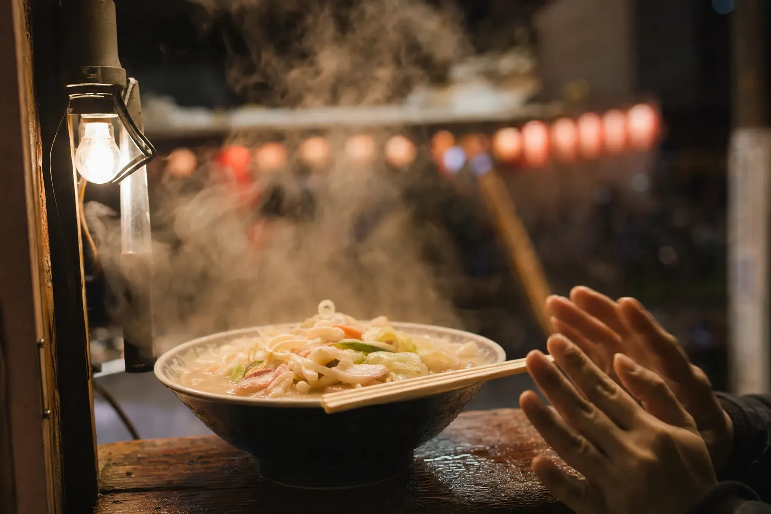 A steaming bowl of Nagasaki champon with rich pork broth at a festival food stall, steam rising into the cold February night air