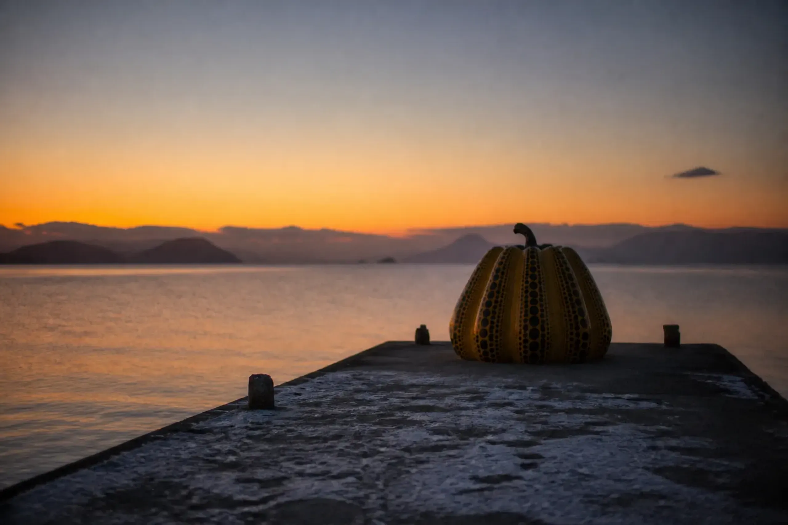 Yayoi Kusama's yellow pumpkin sculpture on the Naoshima pier silhouetted against a fading orange dusk sky over the Inland Sea
