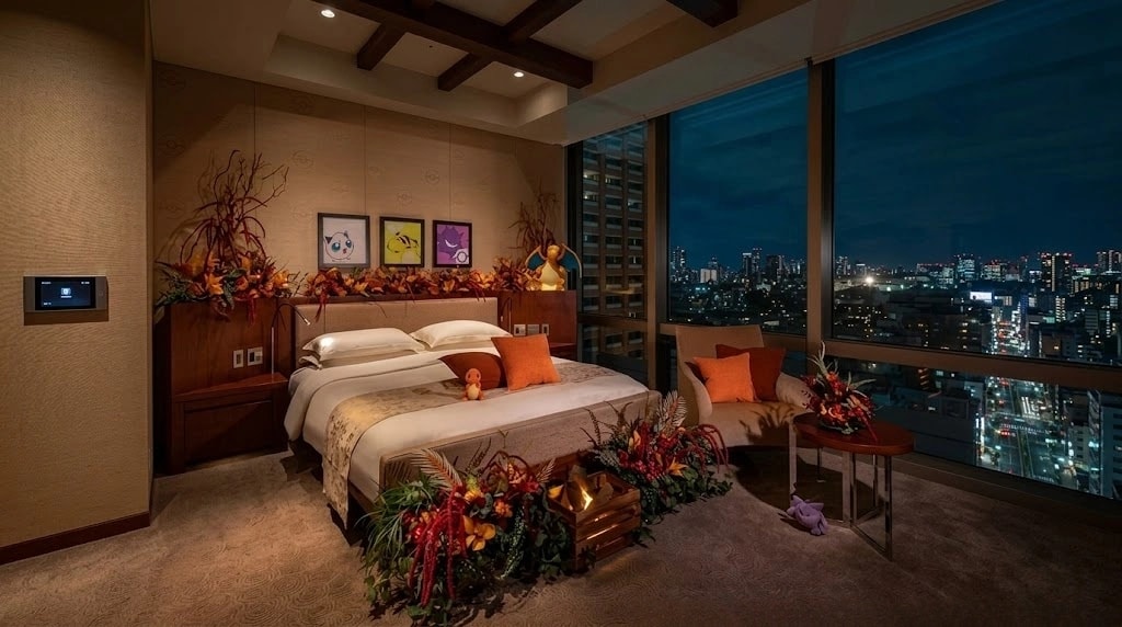 Luxurious hotel room at night with a king bed, autumn floral arrangements, and a floor-to-ceiling cityscape view through large windows.
