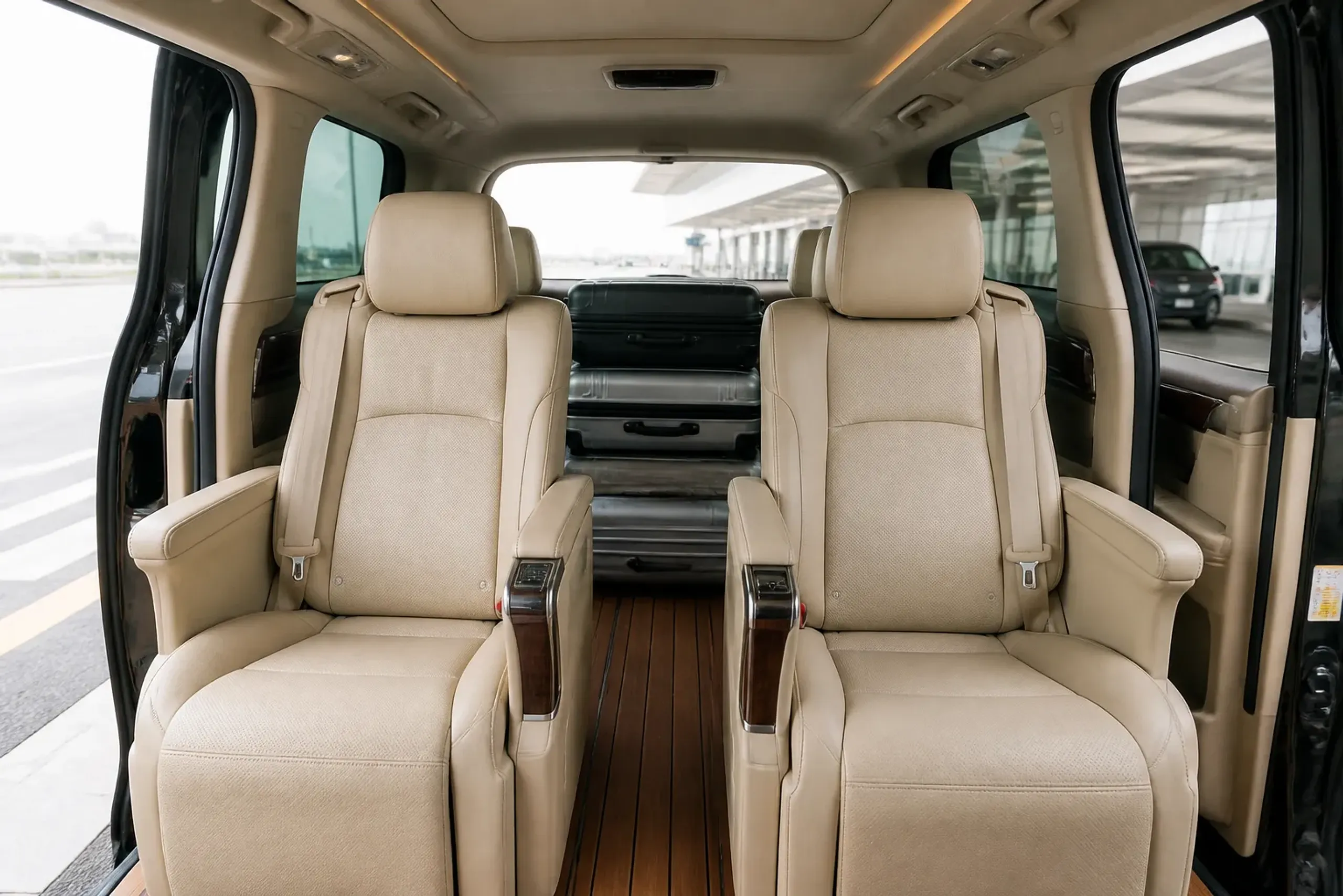Interior of a Toyota Alphard executive van with captain seats and loaded suitcases