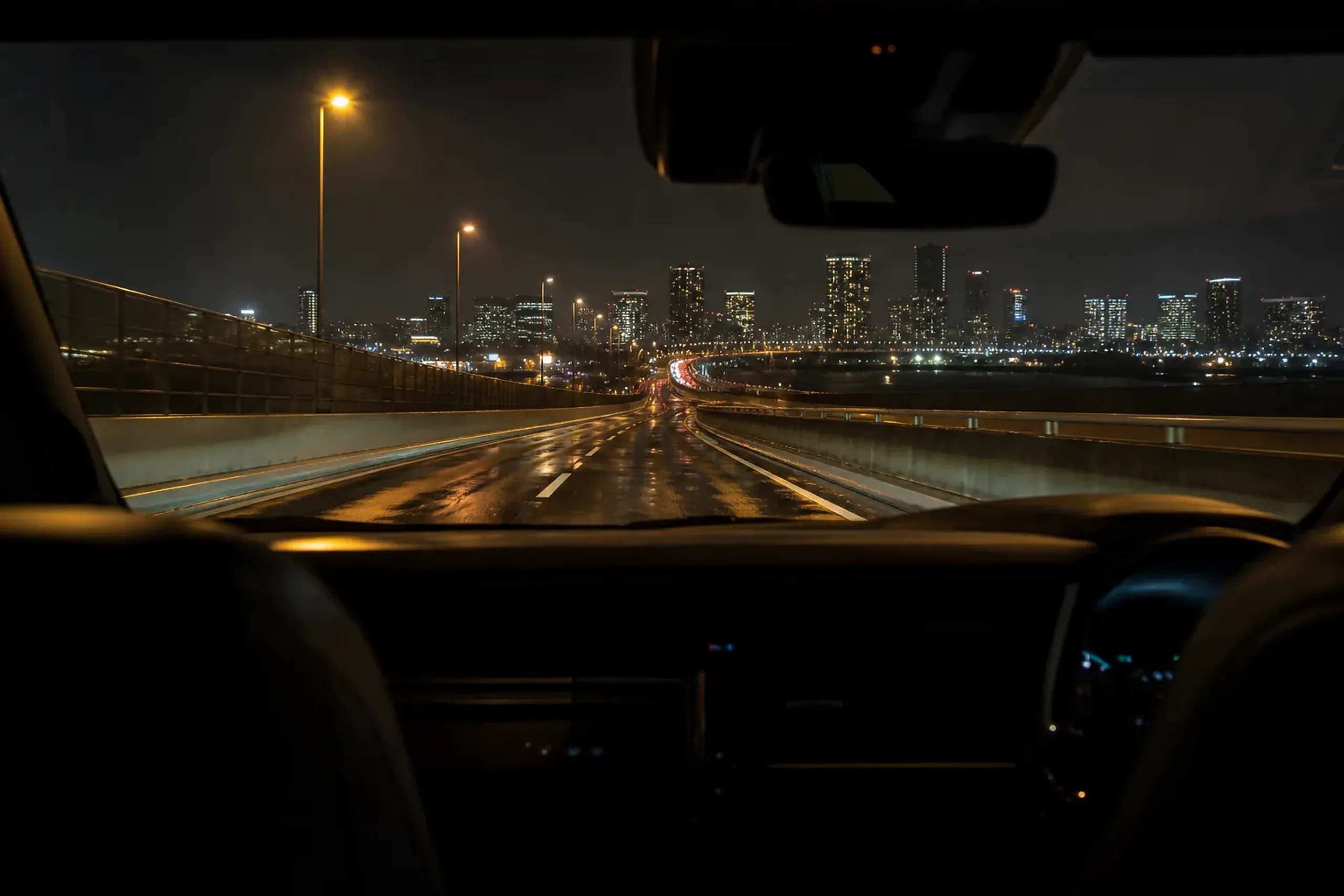 A late-night view of the elevated Shuto Expressway approach from Haneda Airport toward the illuminated skyline of central Tokyo, with clear open lanes
