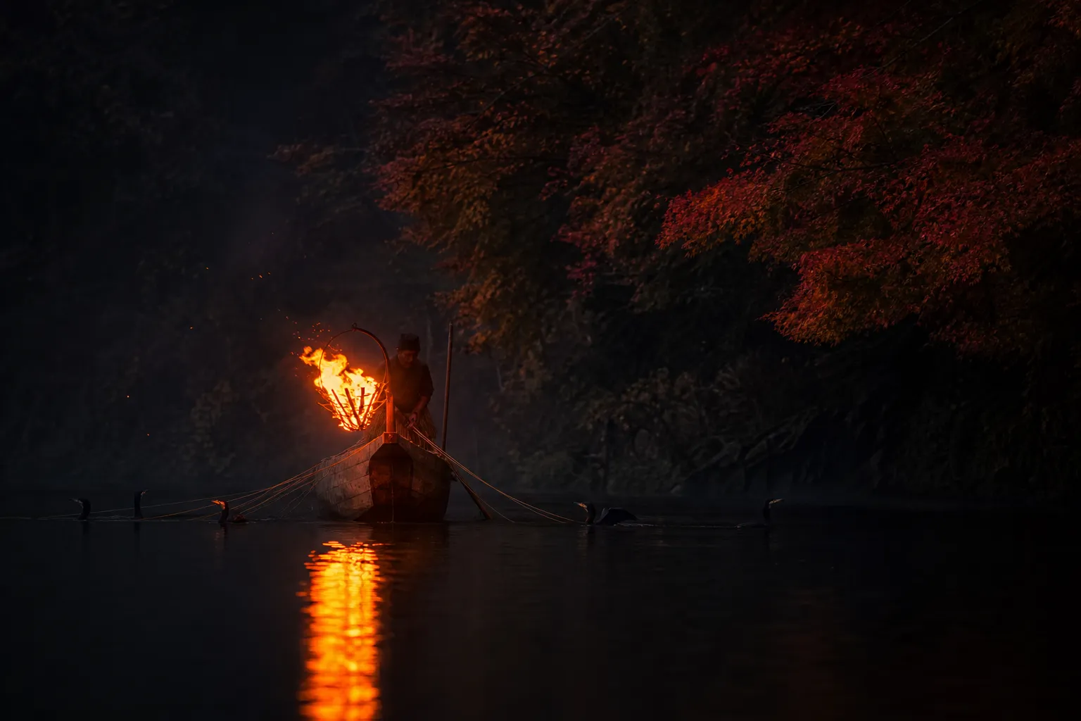 Torchlit wooden boat during ukai on a dark river with reflections on the water