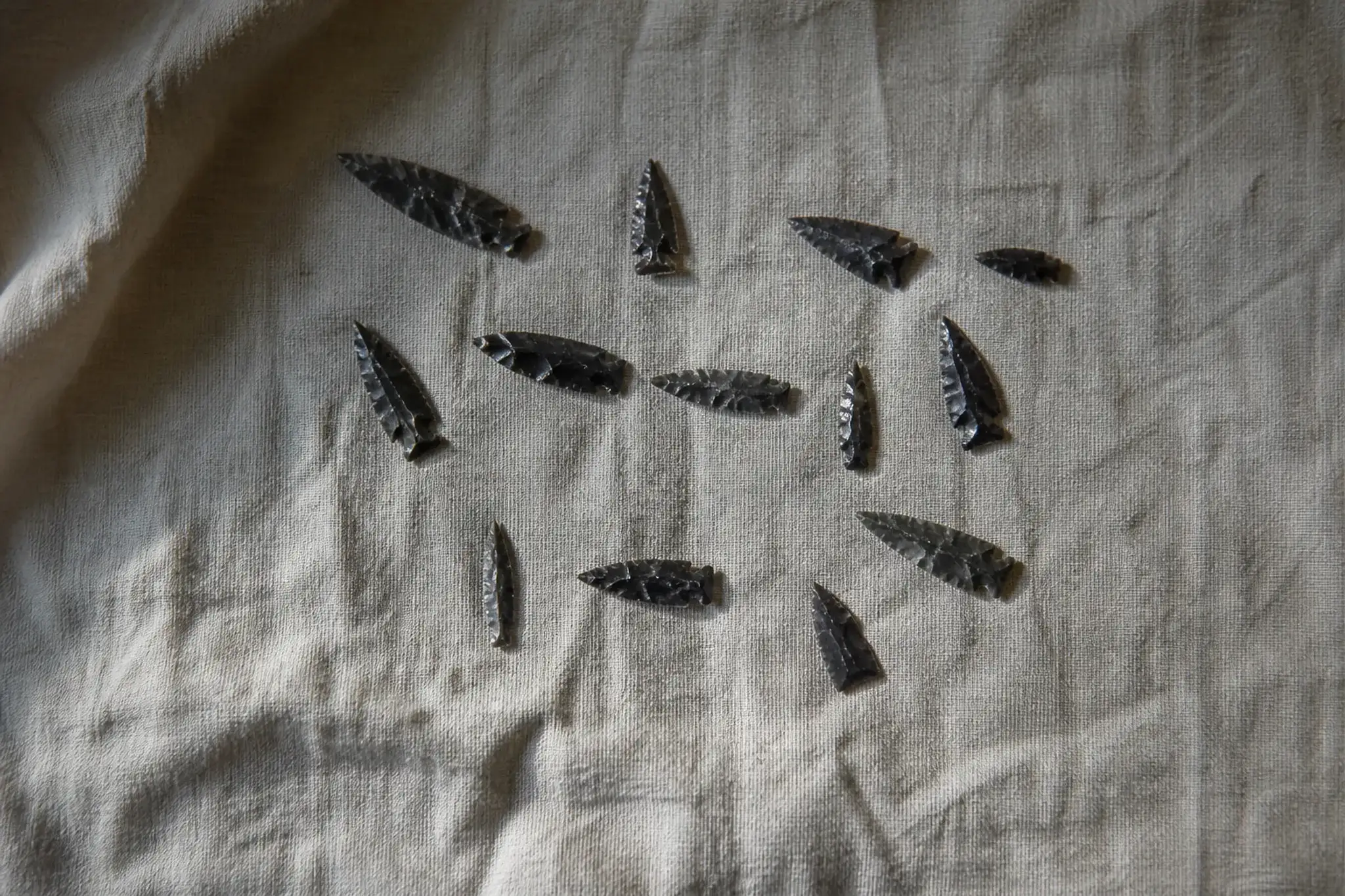 a collection of excavated Palaeolithic and Yayoi sanukite arrowheads, spear points and stone blades with razor-sharp fractured edges laid on cloth