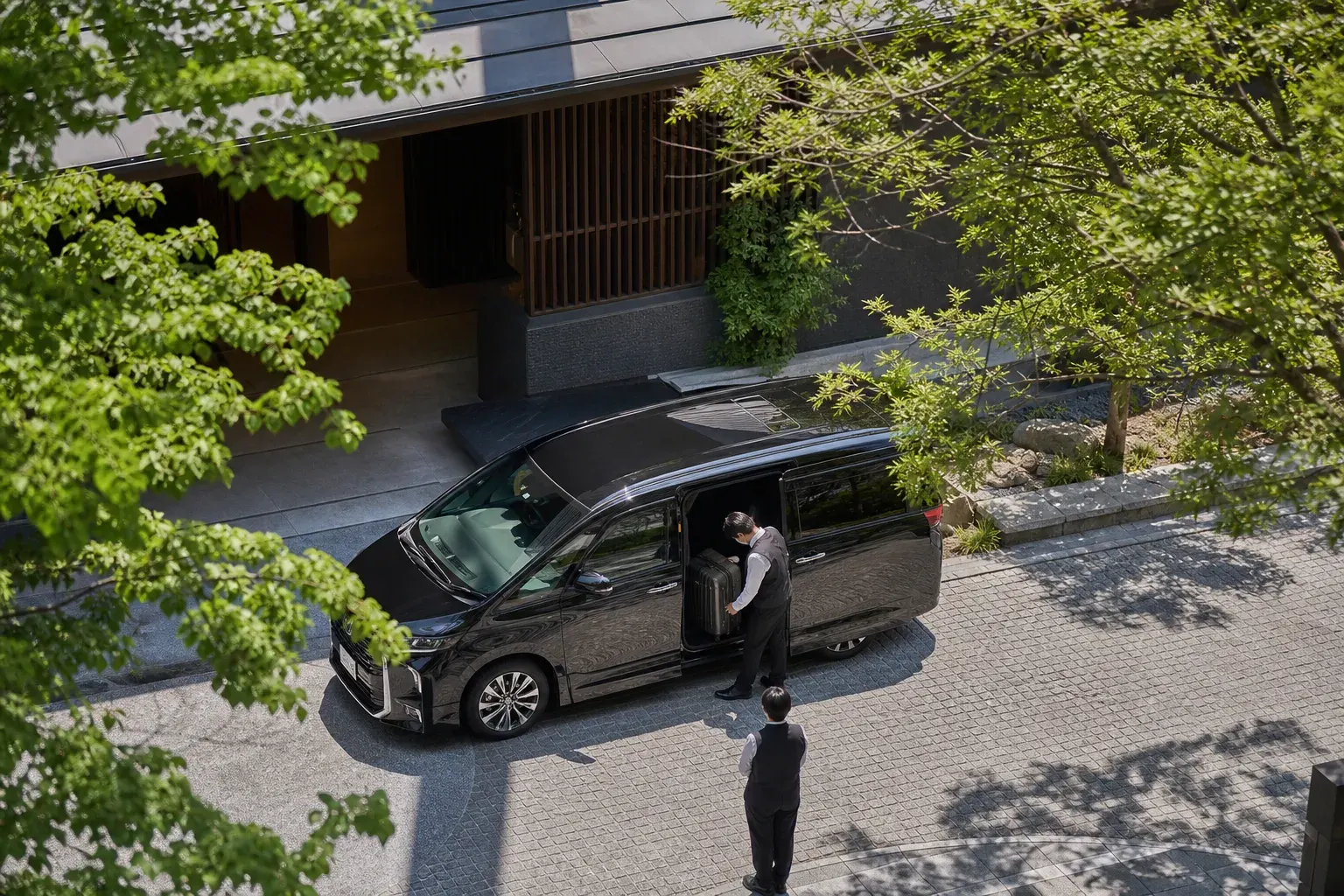 A discreet black chauffeur vehicle outside an Osaka hotel entrance with luggage being loaded