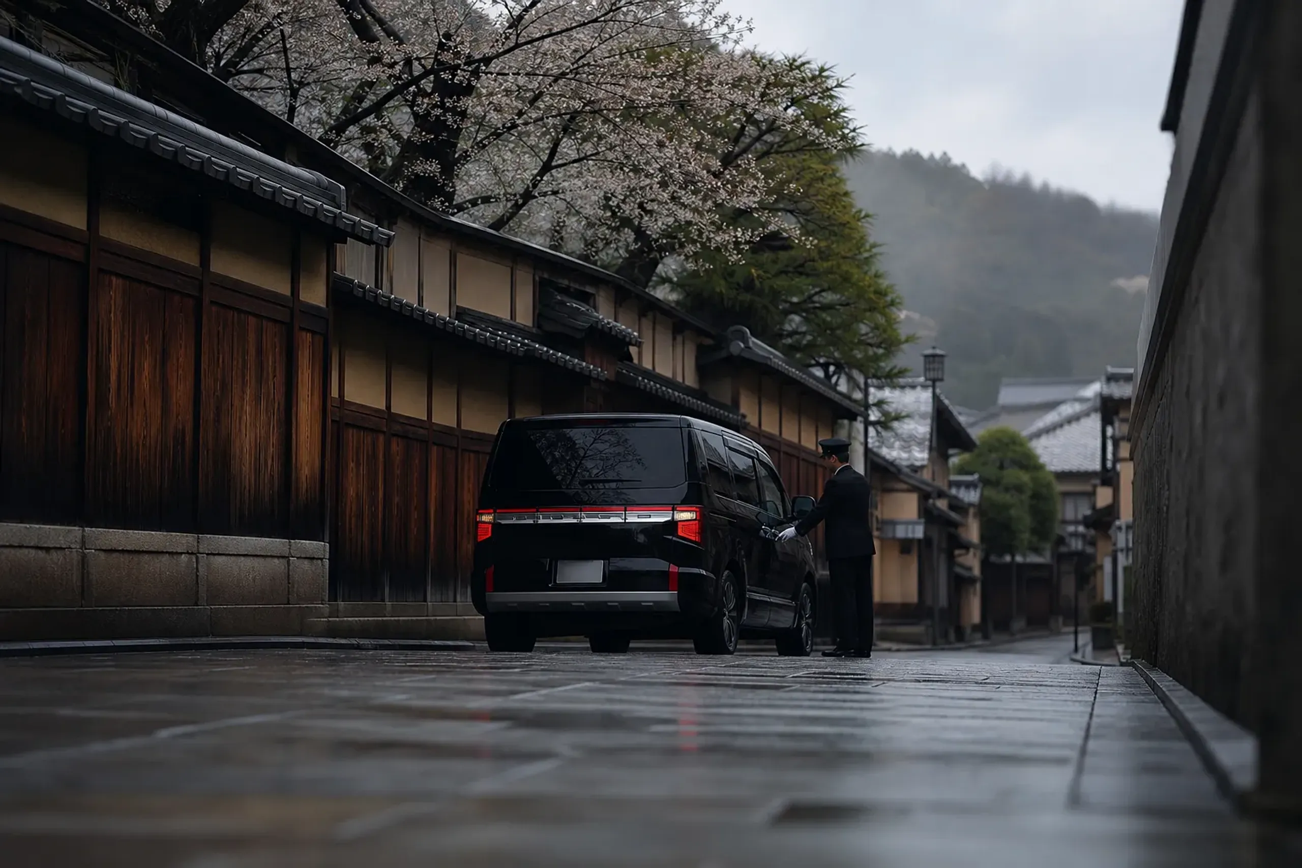 A black luxury minivan and chauffeur on a quiet Kyoto side street, an unmarked private transfer