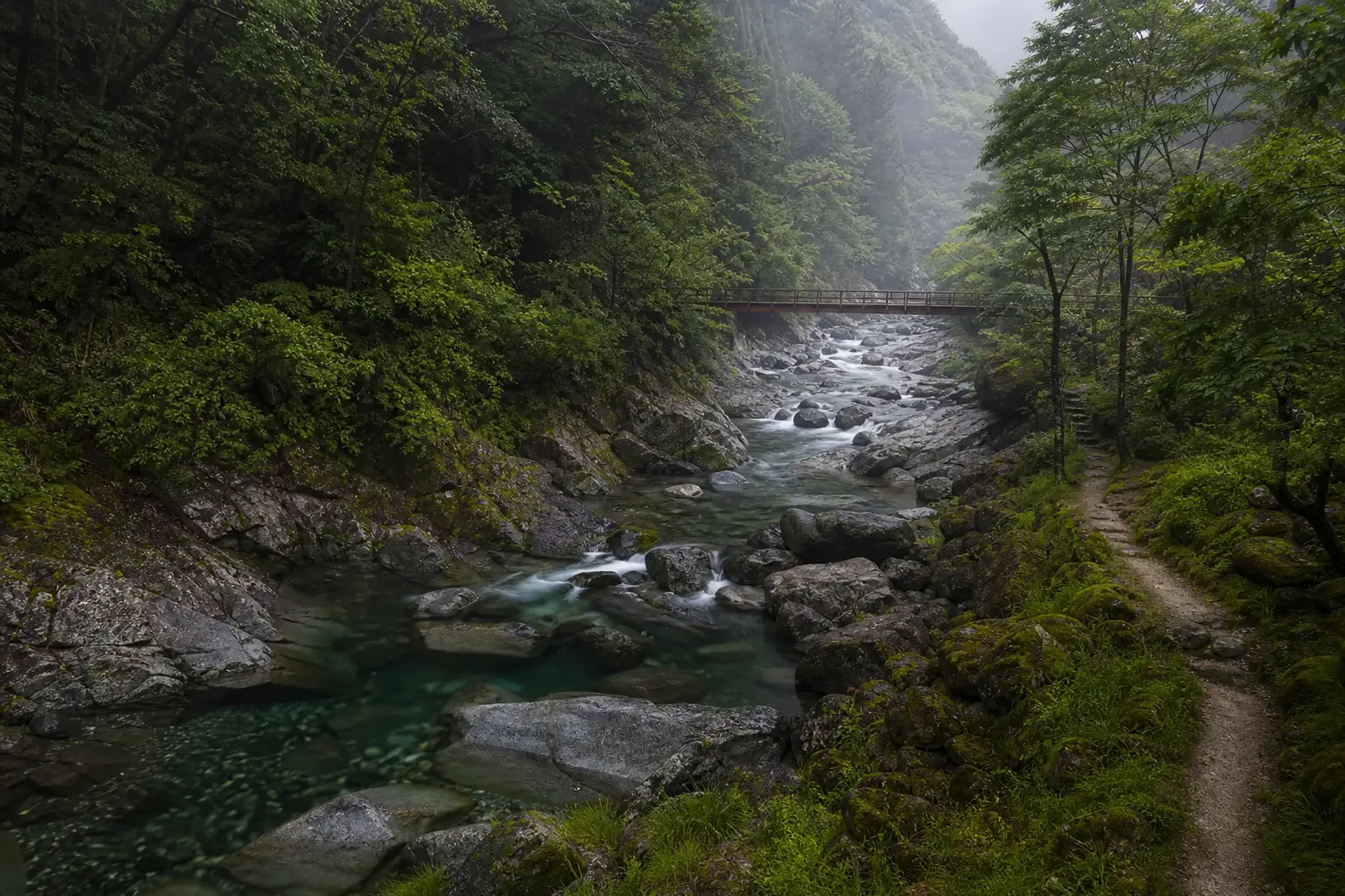 Mountain river valley in Nagano Prefecture during green season with clear stream and forested slopes