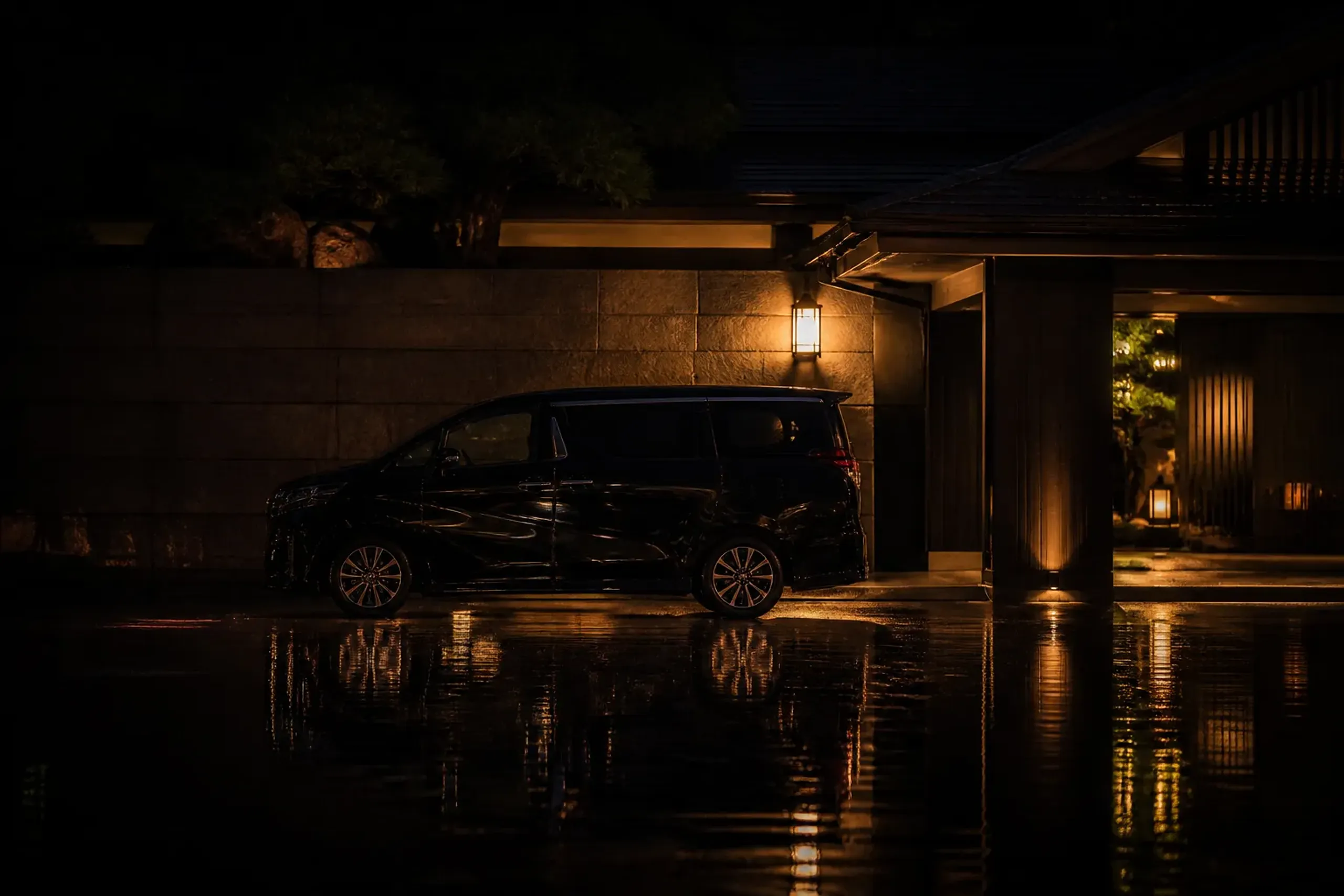 Luxury chauffeur vehicle waiting in a quiet Japanese hotel driveway at night with wet pavement reflections