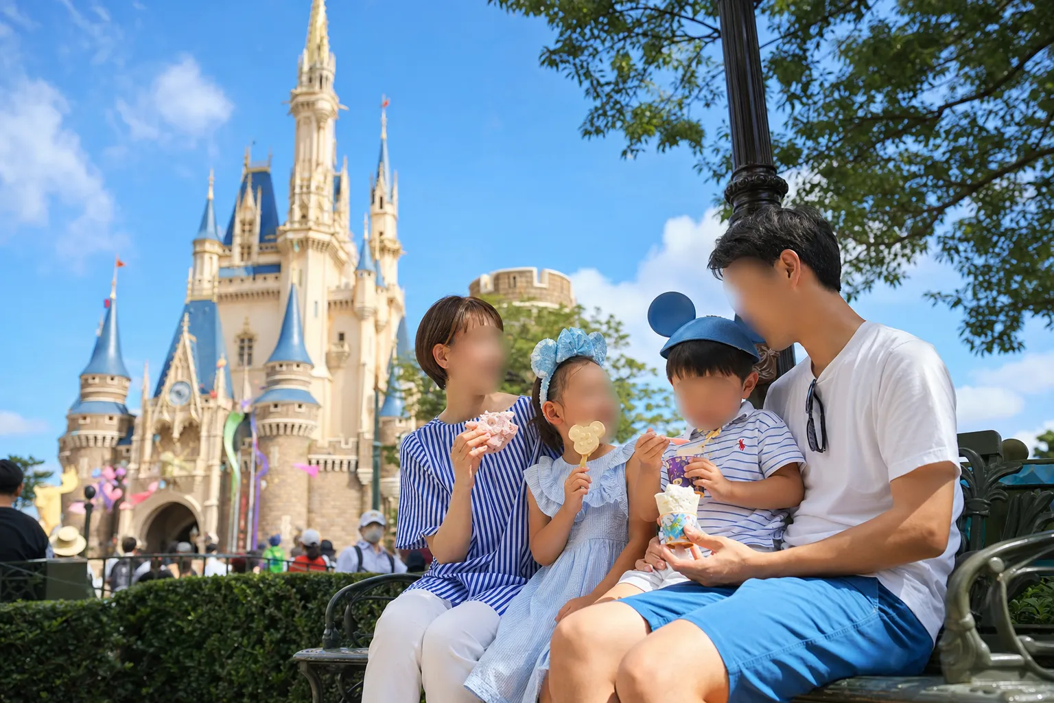 Family with children resting in shade with snacks at a theme park during a busy day