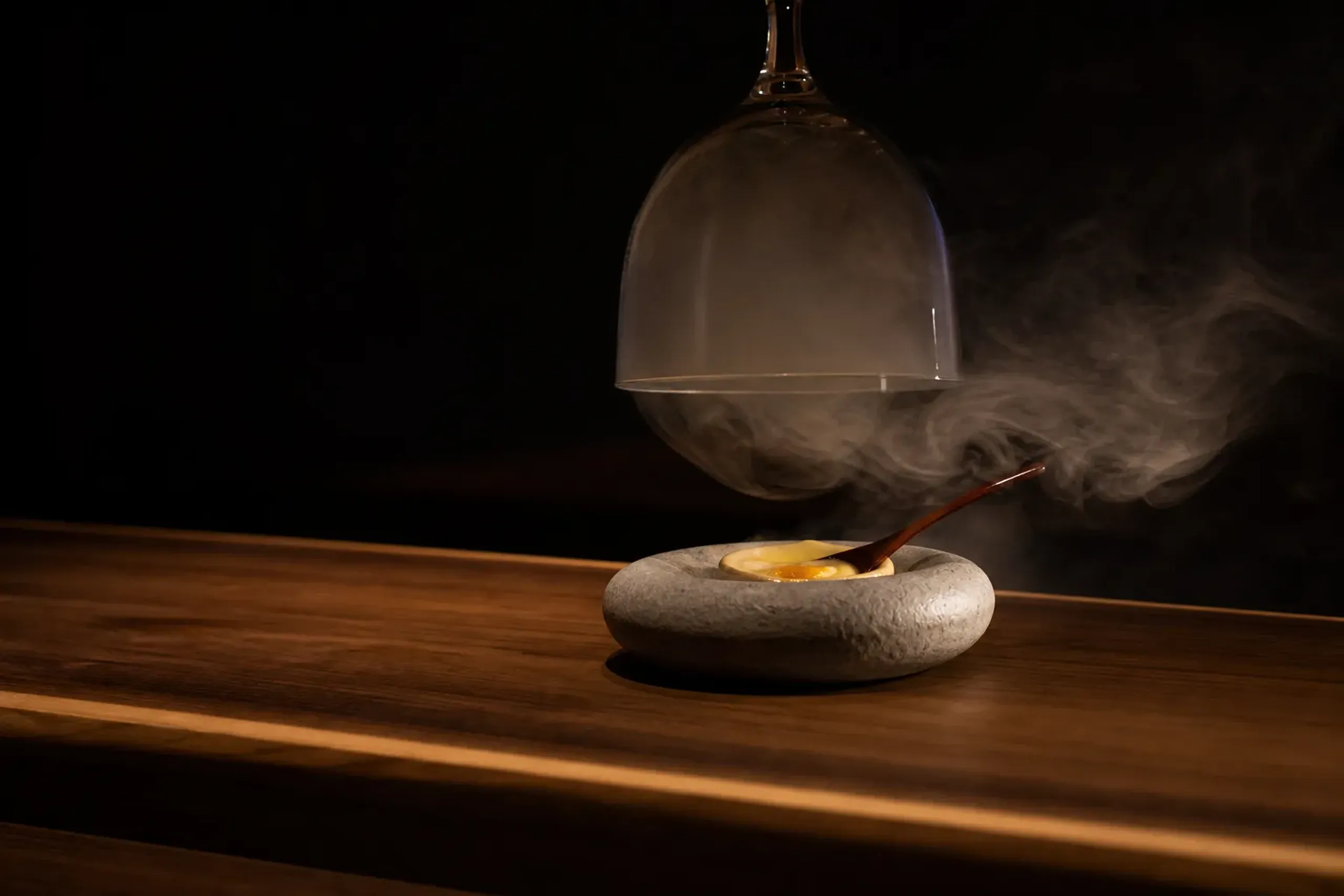 a river-stone-shaped molecular dish releasing thin cedar-scented smoke as its glass cloche is lifted, warm custard center revealed under a spoon at an intimate Tokyo dining counter
