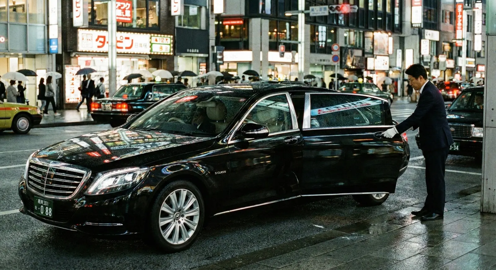 Chauffeur opening the door of a black luxury limousine in Tokyo at night.