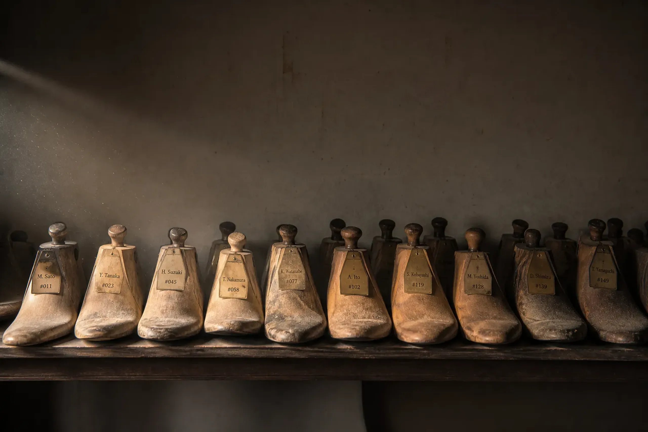 Wooden bespoke shoe lasts stored on a workshop shelf, each labelled per client