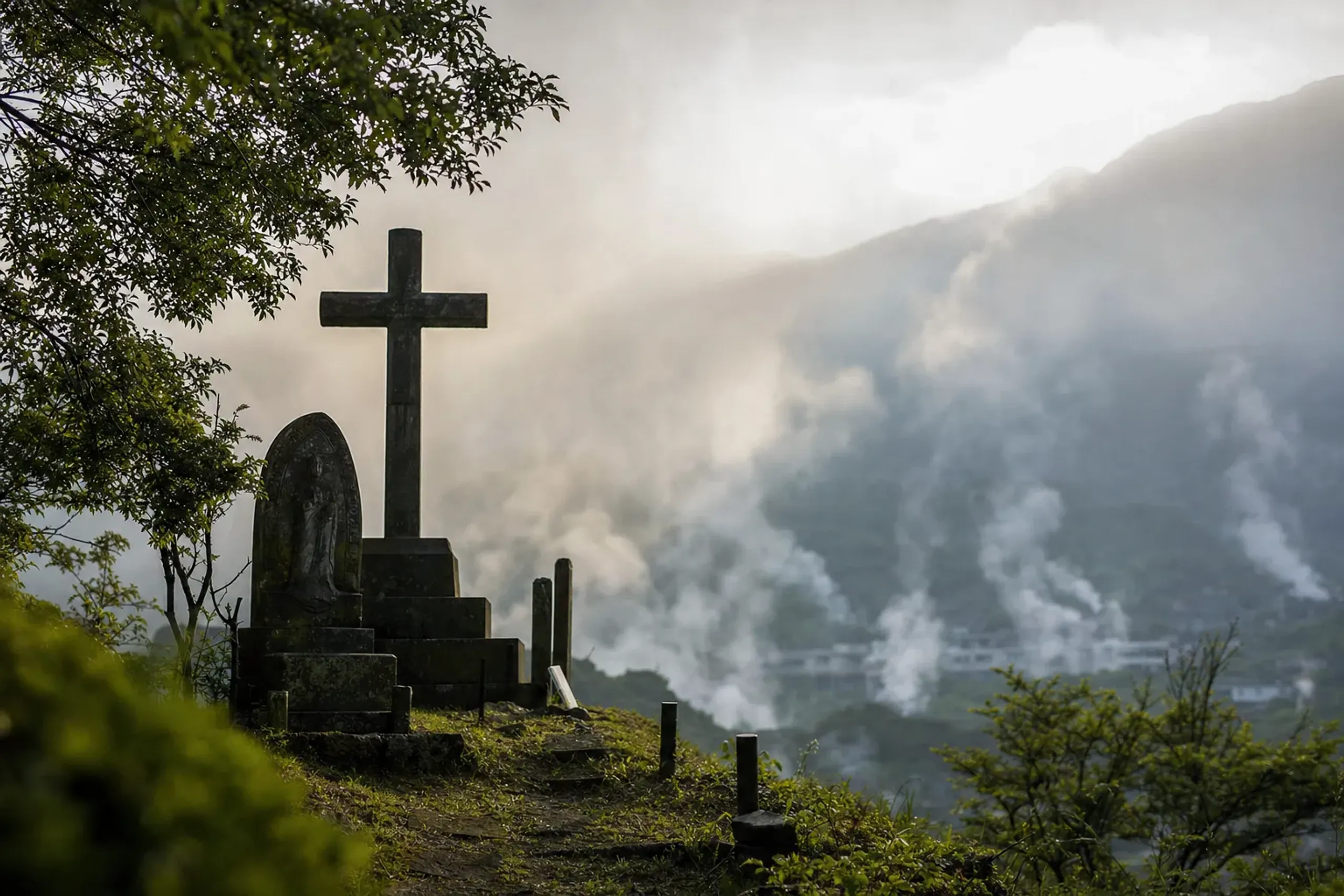 The memorial cross and martyrs' monument standing on the knoll overlooking the steaming vents of Unzen Jigoku