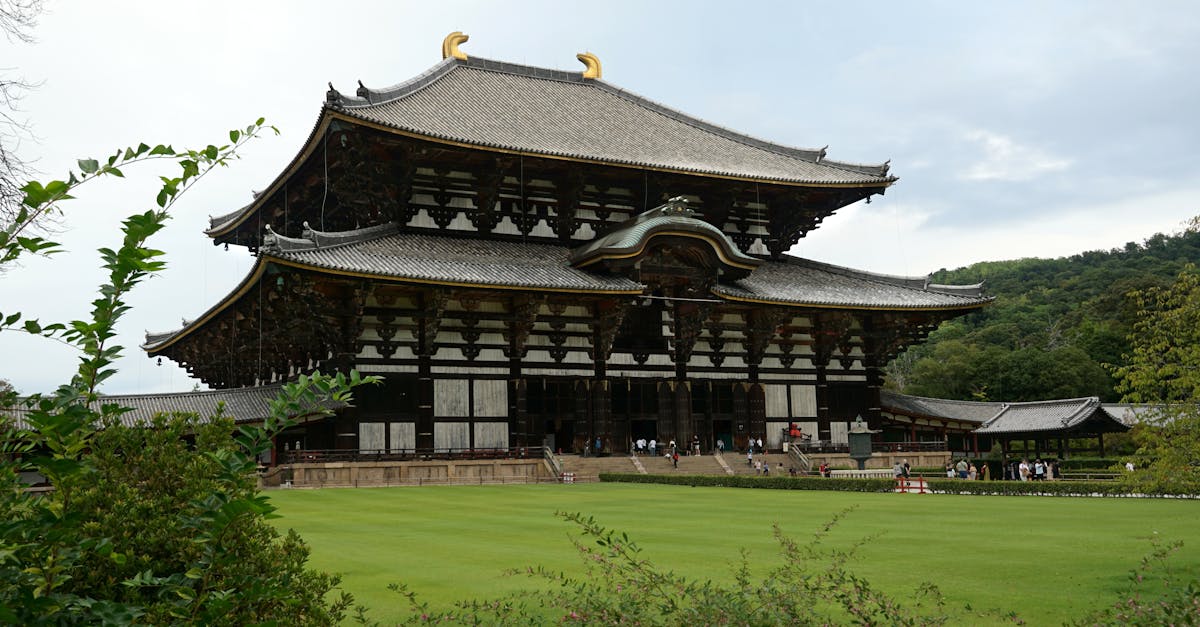 Large traditional Japanese temple with multi-tiered, curved tiled roofs and wooden latticework, set in front of a manicured lawn and visitors at the entrance.