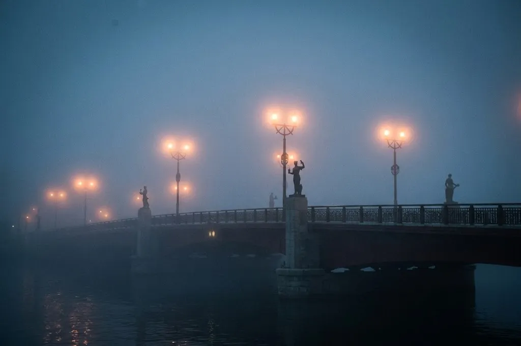 Dense white sea fog blankets the Nusamai Bridge in Kushiro, with glowing streetlamps piercing through the mist, creating a mysterious and enchanting atmosphere over the quiet Kushiro River.