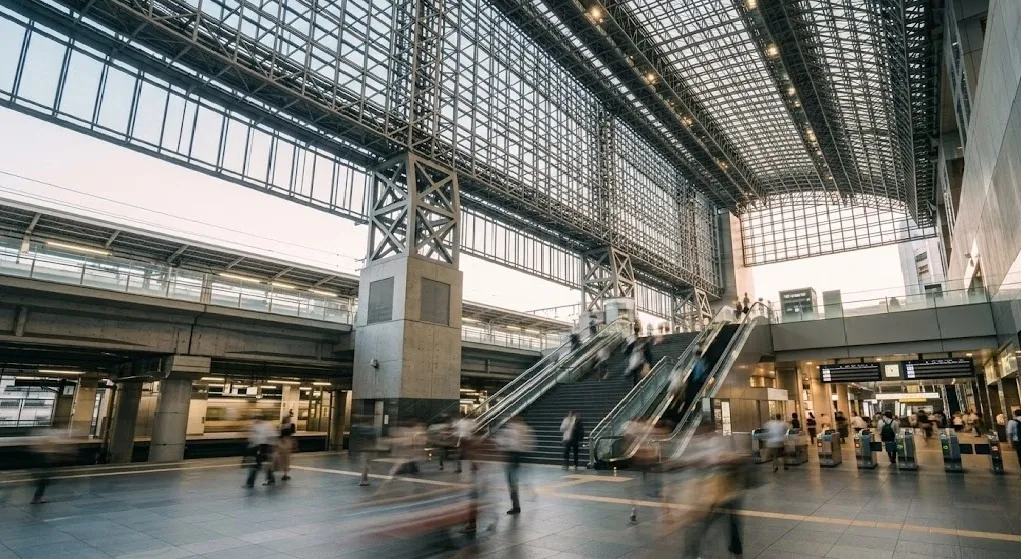 A sophisticated long-exposure photograph capturing the dynamic motion of commuters at Kyoto Station, where blurred figures signify the intense energy and volume of morning peak travel times.