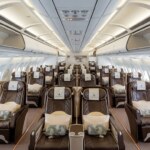 Interior of a modern airplane cabin with many brown leather seats and overhead bins.