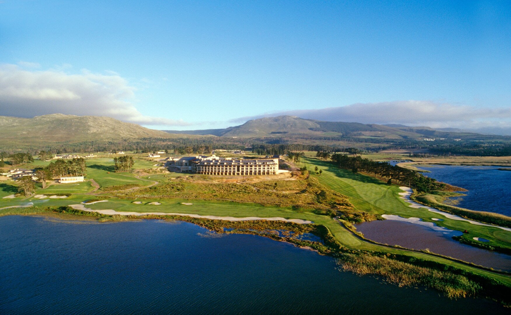 Aerial shot of a luxury golf resort situated next to a large lagoon and rolling mountains.